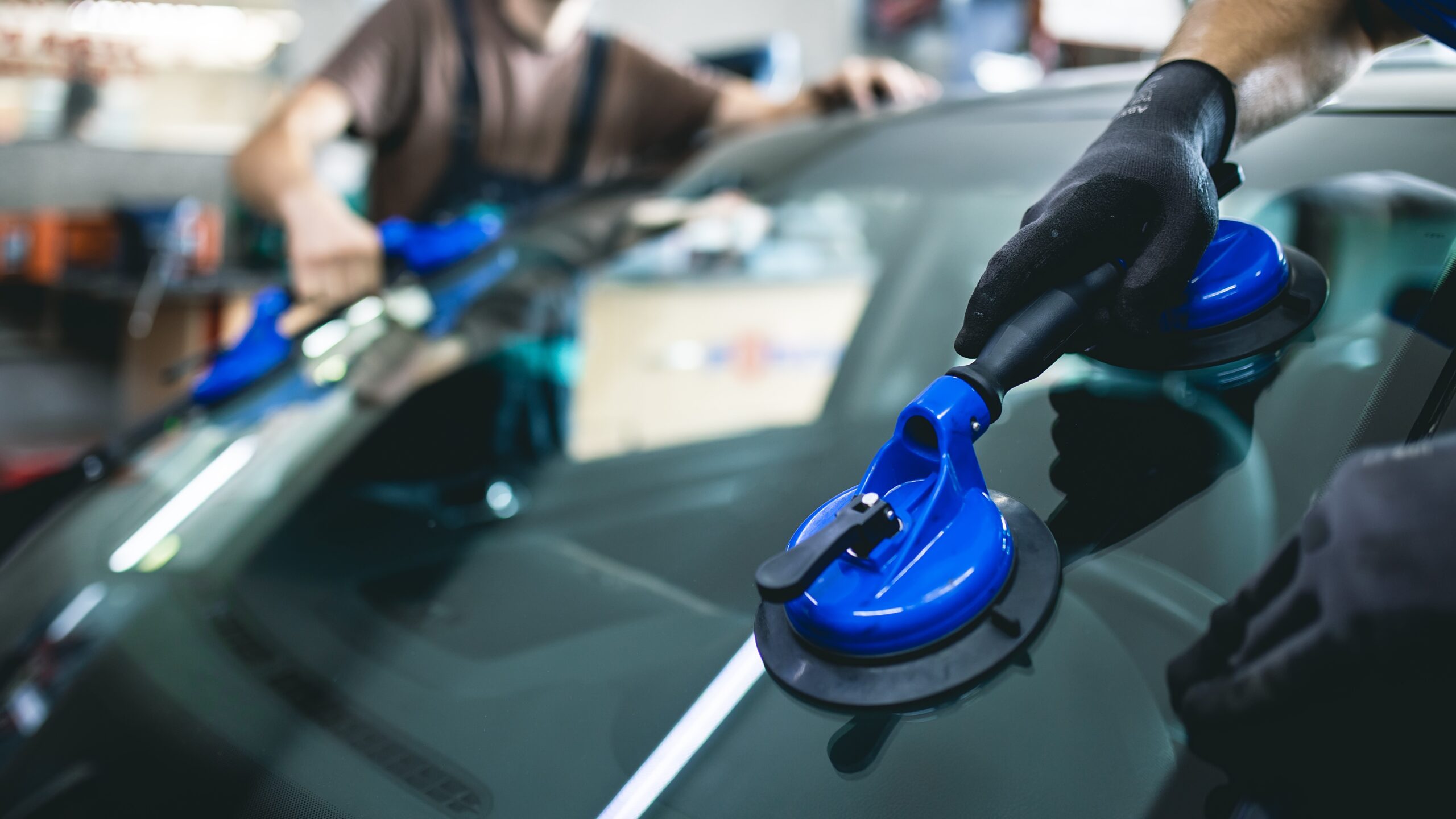 Close view of two technicians in a shop sliding a replacement windshield into place.