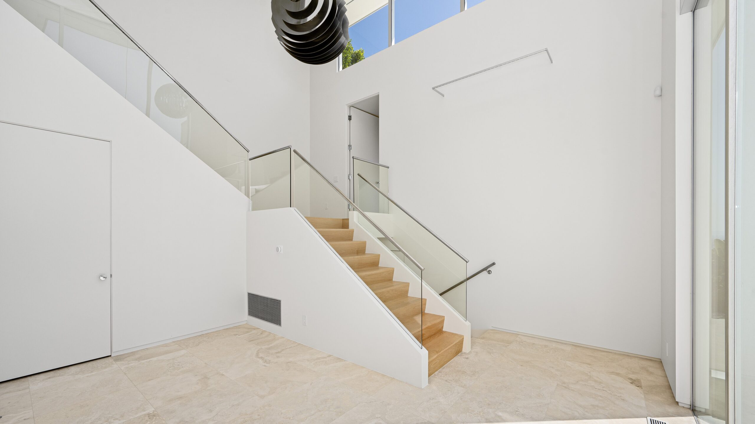 Interior view of sleek modern home with white walls, wooden stairs, and new glass railings