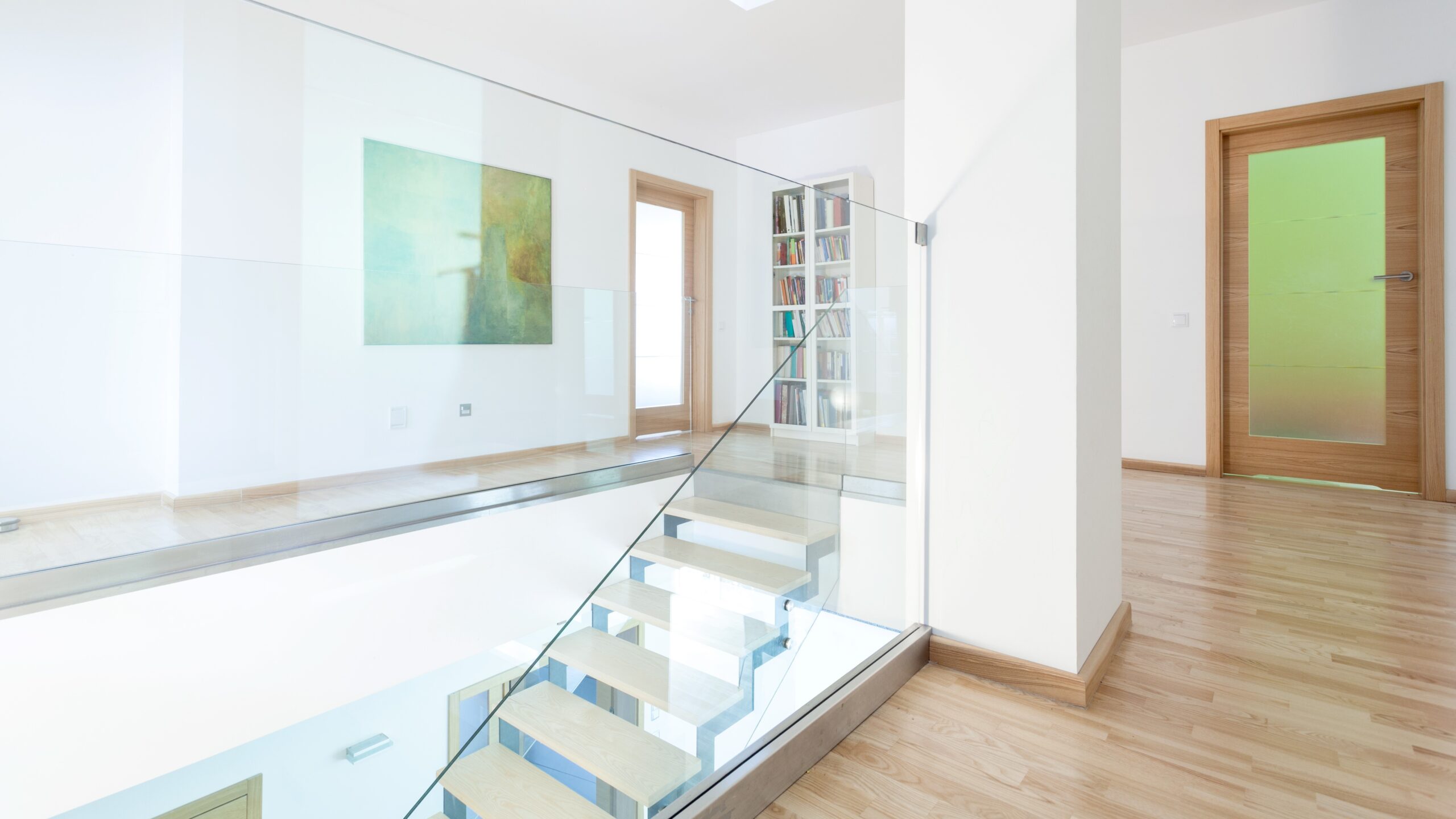 Second story of modern home with hardwood flooring, white walls, and newly installed glass railing on a staircase